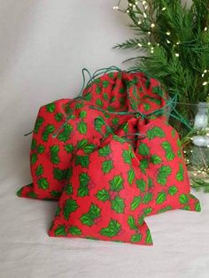 two red bags with green holly designs on them sitting next to a christmas tree branch