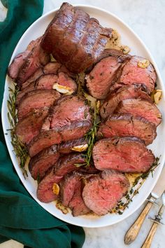 sliced steak on a white plate with green garnish next to utensils