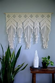 the wall hanging is decorated with tassels and plants in pots next to a wooden table