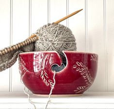 a red bowl with yarn in it and a ball of knitting needles next to it