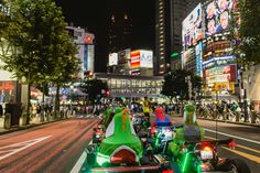 some people are riding motorcycles down the street at night with neon lights on them and buildings in the background