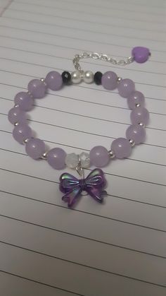 a bracelet with purple beads and a butterfly charm on it's side, sitting on top of lined paper