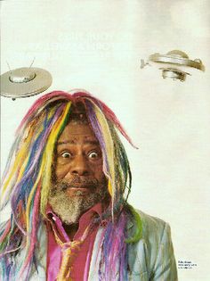 a man with multicolored dreadlocks standing in front of a white background