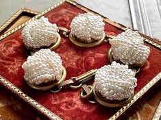 four white beaded buttons sitting on top of a red velvet box with gold trim