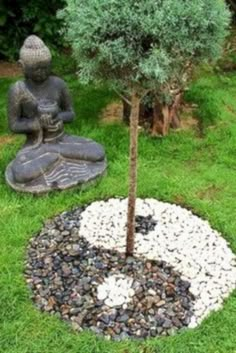 a buddha statue sitting next to a small tree in the middle of a garden area