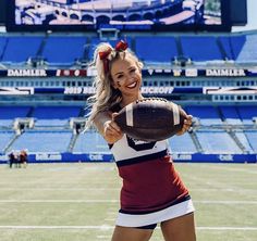 a beautiful young woman holding a football on top of a field in front of an empty stadium