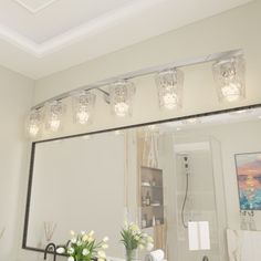 a bathroom mirror with lights above it and flowers in vases on the counter top