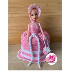 a crocheted doll is wearing a pink dress and hat with white trims