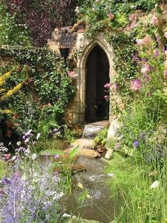 a garden with lots of flowers and plants around the entrance to an old stone building