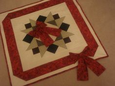 a red and white quilted table topper with bows on the edge, sitting on a beige surface