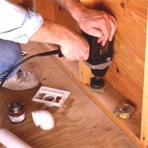 a man using a drill to fix a hole in the wall under a cabinet door