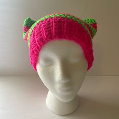 a white mannequin head wearing a pink and green knitted hat with ears