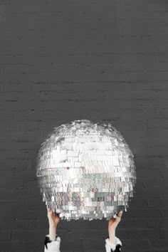 a person holding up a disco ball in front of a brick wall