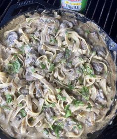 a skillet filled with pasta and mushrooms on top of a grill next to a bottle of beer