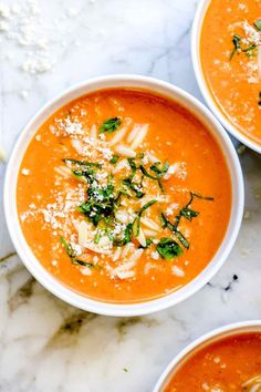 three bowls of tomato soup topped with parmesan cheese