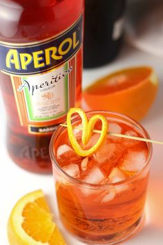 an orange drink is garnished with lemon wedges next to a bottle of aperol