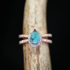 a ring with a turquoise stone surrounded by white diamonds on top of a piece of wood