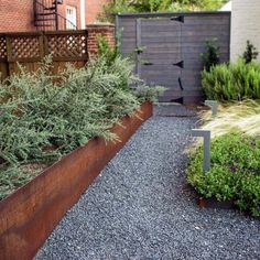 a long metal planter filled with plants next to a brick wall and wooden fence