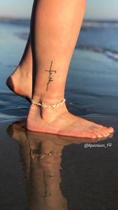 a woman's foot with a cross tattoo on it and water in the background