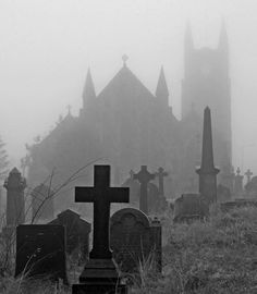 black and white photograph of graveyard with church in the background on a foggy day