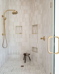 a walk in shower sitting next to a white tiled wall and floor with gold fixtures