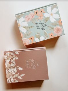 two boxes with floral designs on them sitting next to each other, one has a note in it