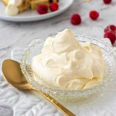 a glass bowl filled with whipped cream and raspberries next to a gold spoon