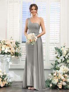 a woman standing in front of flowers wearing a gray bridesmaid dress and holding a bouquet