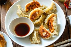 some dumplings are on a white plate with sauce and chopsticks next to them