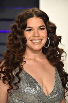 a woman with long curly hair wearing a silver dress