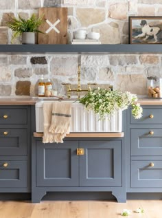 a kitchen with blue cabinets and stone wall behind the countertop is decorated with greenery