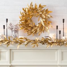 a wreath on top of a mantle next to candles and other decorating items in front of a white painted wall