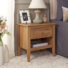 a night stand with a lamp on it next to a bed and flowers in vases