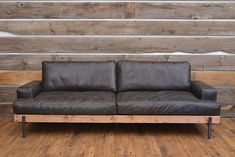 a black leather couch sitting on top of a wooden floor next to a wood wall