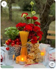 a table topped with lots of red flowers next to candles and plates filled with food