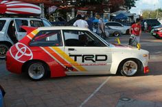 a white car with red, yellow and orange stripes parked in a parking lot next to other cars