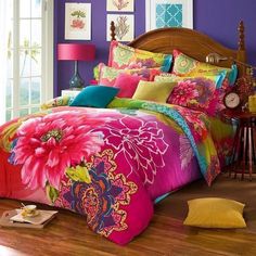 a bed with colorful comforters and pillows in a room next to a lamp on a table