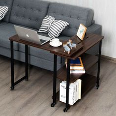 a laptop computer sitting on top of a wooden table next to a gray couch with black and white pillows