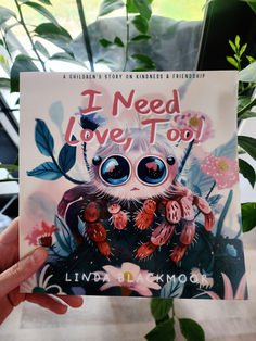 a person holding up a book about i need love to go with plants in the background