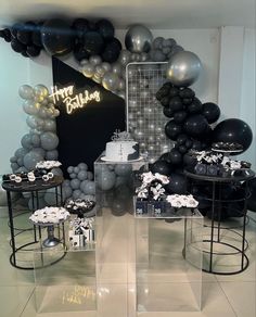 a room filled with black and white balloons, cake and other items on tables in front of a sign that says happy birthday