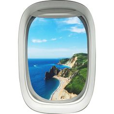 an airplane window looking out at the ocean and cliffs on the coast below it, with blue sky and white clouds