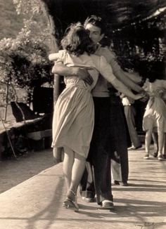 an old black and white photo of two people holding each other's arms as they walk down a sidewalk