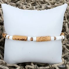 a white pillow with a wooden beaded bracelet on it's end, sitting next to a cushion