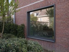 a brick building with a large window on the side and bushes in front of it