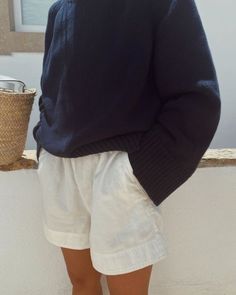 a woman in shorts and a sweater standing by a window