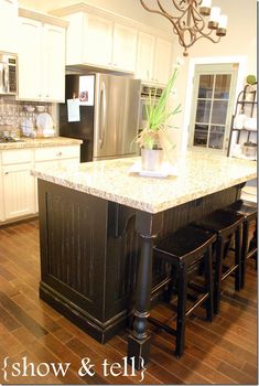 an island in the middle of a kitchen with stools and a chandelier