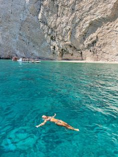 a person swimming in the ocean near a cliff