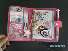 a hand holding a pink case filled with assorted items on top of a table