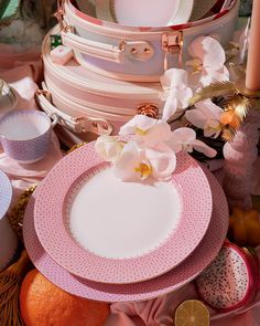 a stack of pink and white plates sitting on top of a table next to oranges