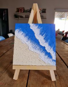 an easel sitting on top of a wooden table with a painting in the middle